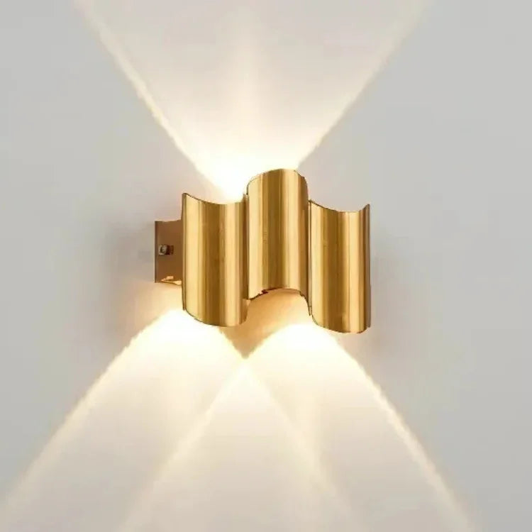 Modern gold wall sconce with wavy design, casting warm up and down light on white wall
